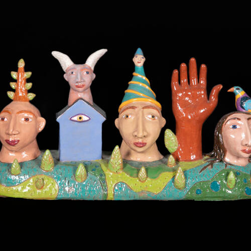 Colorful ceramic sculpture that has three heads, a house, and a hand situated on a base with elements of a landscape, like trees and blue water.